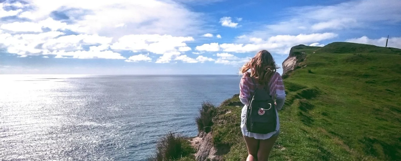 woman standing on cliff near body of water during daytime