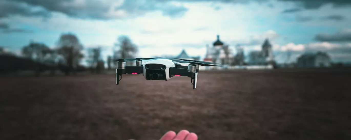 white and black drone flying over the field during daytime