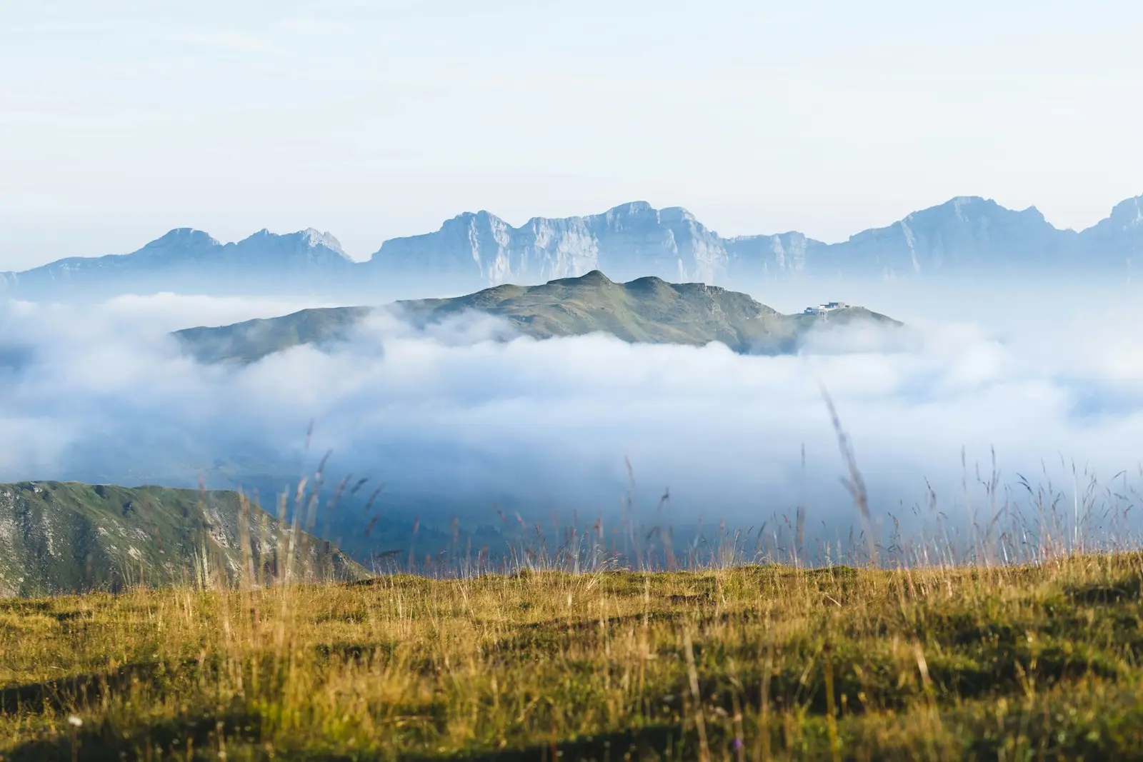 Mountains rise above clouds with a grassy foreground.
